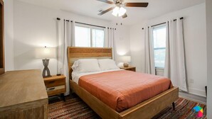 A bedroom with a wooden bed, two bedside tables, a ceiling fan, and a window with curtains.