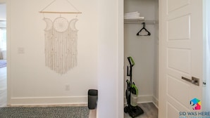 A room with a wall-mounted macrame piece, a vacuum cleaner, and a door leading to a closet.