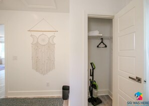 A room with a wall-mounted macrame piece, a vacuum cleaner, and a door leading to a closet.