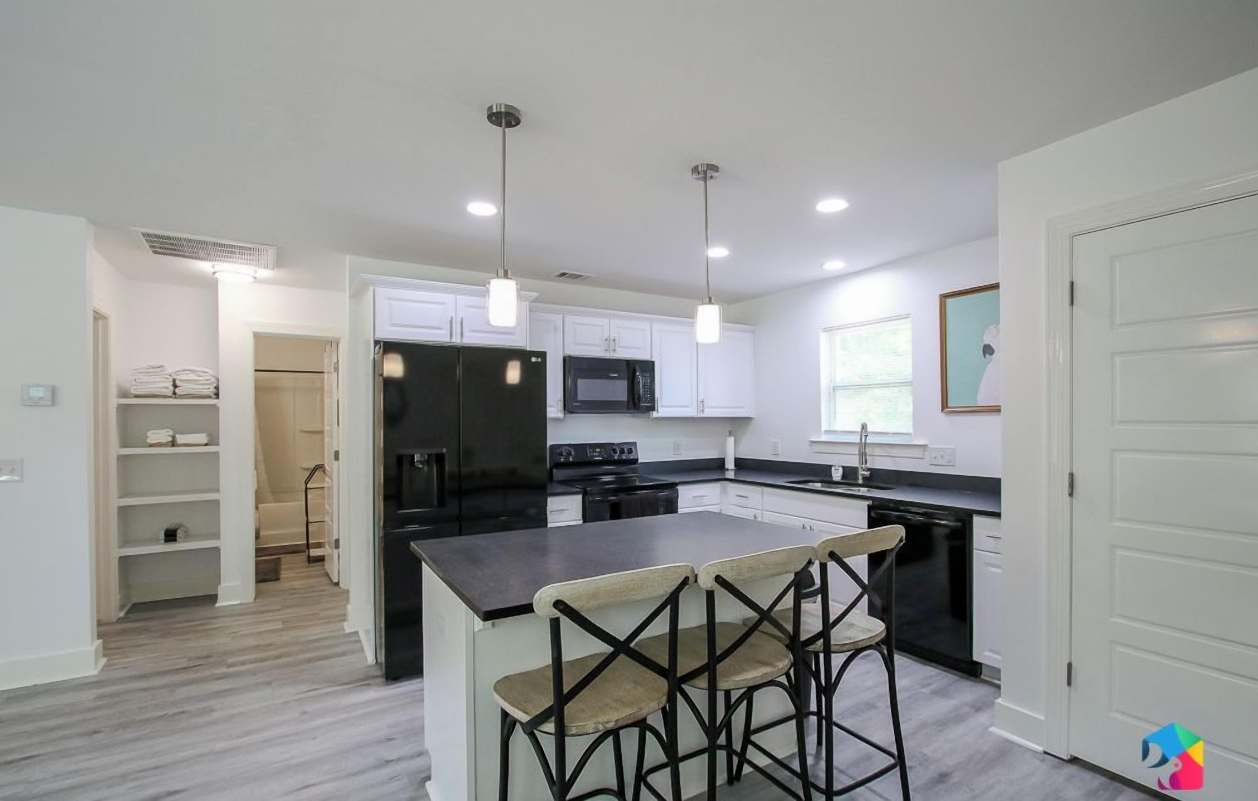 A modern kitchen with white cabinets, a black refrigerator, a microwave, and a stove. There are three bar stools at the island.