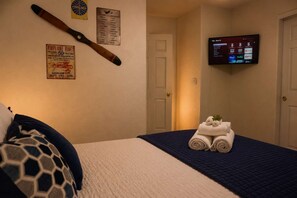Une chambre d’hôtel avec un lit, un téléviseur fixé au mur et une affiche accrochée au mur.
