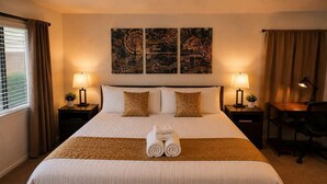 Habitación de hotel con una cama grande, dos mesitas de noche con lámparas, un escritorio y una silla. Hay dos obras de arte colgadas en la pared sobre la cama.