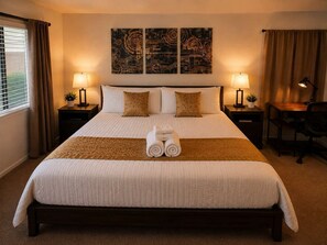 A hotel room with a large bed, two bedside tables with lamps, a desk, and a chair. There are two wall-mounted artworks above the bed.