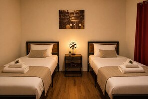Una habitación de hotel con dos camas, una mesita de noche con lámpara y un cuadro en la pared.
