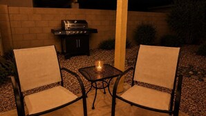 Un espacio al aire libre con dos sillas, una mesa, una parrilla y un pilar.
