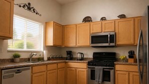 Una cocina con armarios de madera, electrodomésticos de acero inoxidable, lavavajillas y una ventana con persianas.