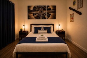 A hotel room with a large bed, two bedside tables, a wall clock, and a painting above the bed.