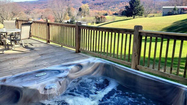 Een hottub op een houten terras met uitzicht op een berg en een huis op de achtergrond.