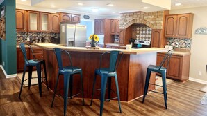 Een keuken met een centraal eiland, barstoelen, houten kasten, een koelkast, een fornuis en een decoratieve spatwand.
