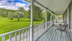 A covered porch with a view of a green lawn and trees.
