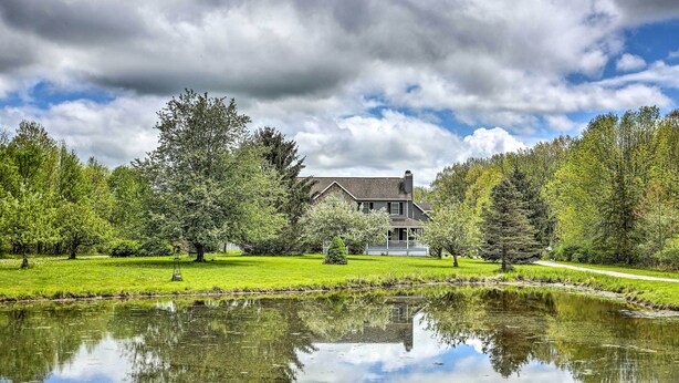 A house with a pond in front, surrounded by trees and a clear sky.