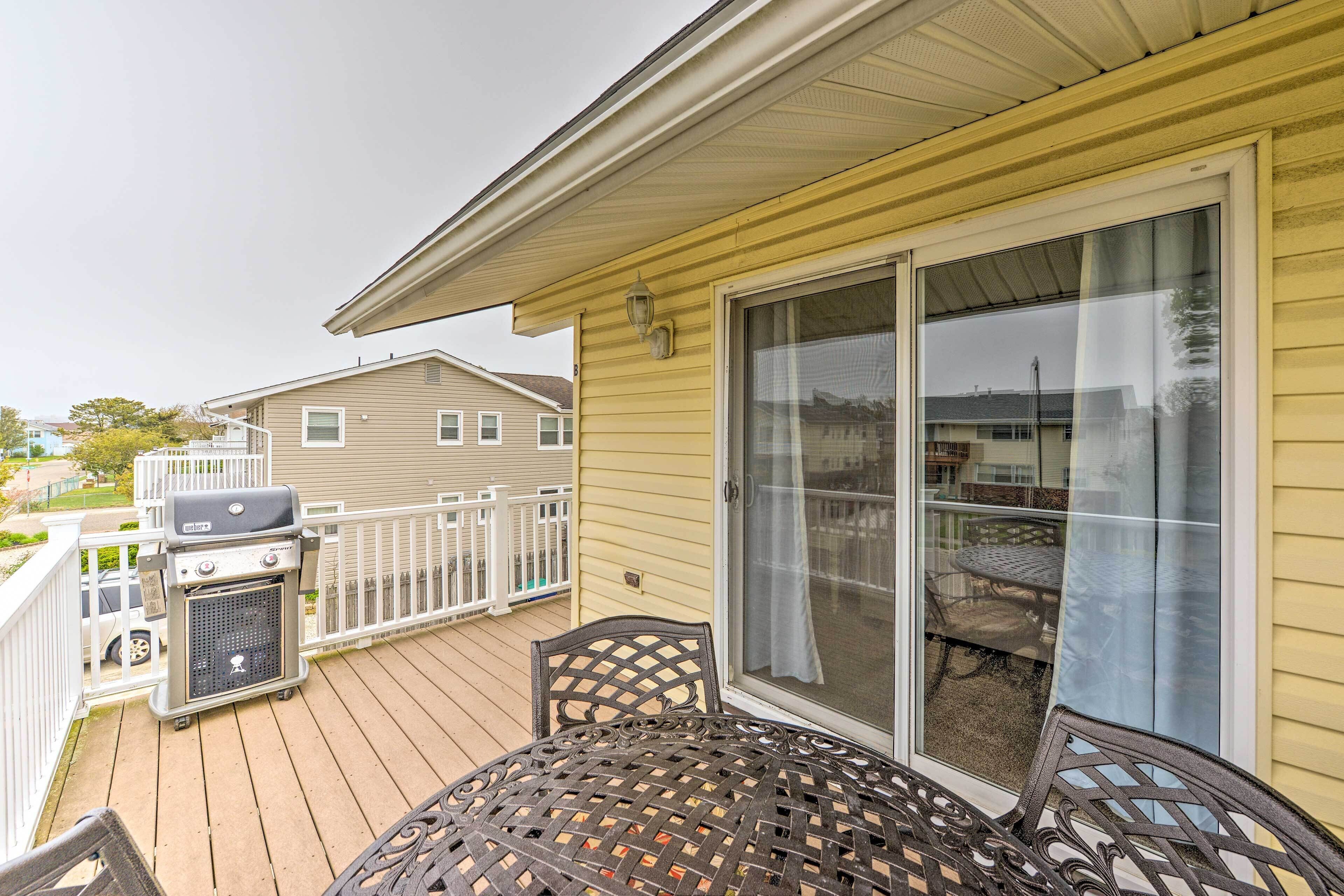 A covered outdoor area with a patio table and chairs, a barbecue grill, and a sliding glass door leading to an outdoor seating area.