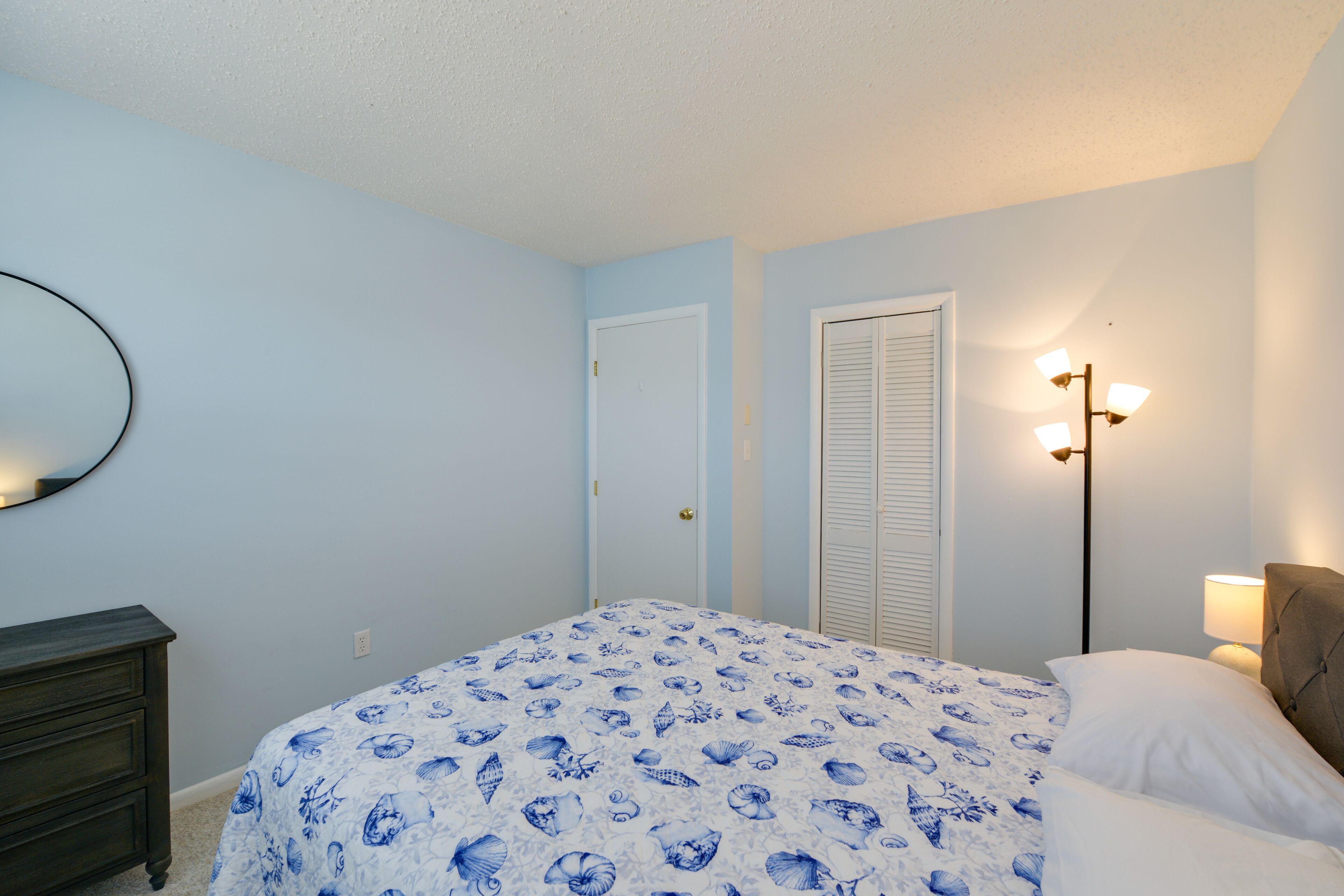 Un dormitorio con cama, cómoda y lámpara de pared.