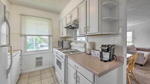 A compact kitchen with white cabinets, a stove, microwave, and a coffee maker. - Brigantine Condo w/ Gas Grill - Walk to Beach! (Brigantine)