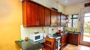 A kitchen with wooden cabinets, a microwave, a gas stove, and a sink. - Captivating 2-Bed Cottage in Kampala (kampala)