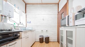 Una cocina compacta con estufa, microondas y armarios. Hay dos botes de basura y piso de madera.