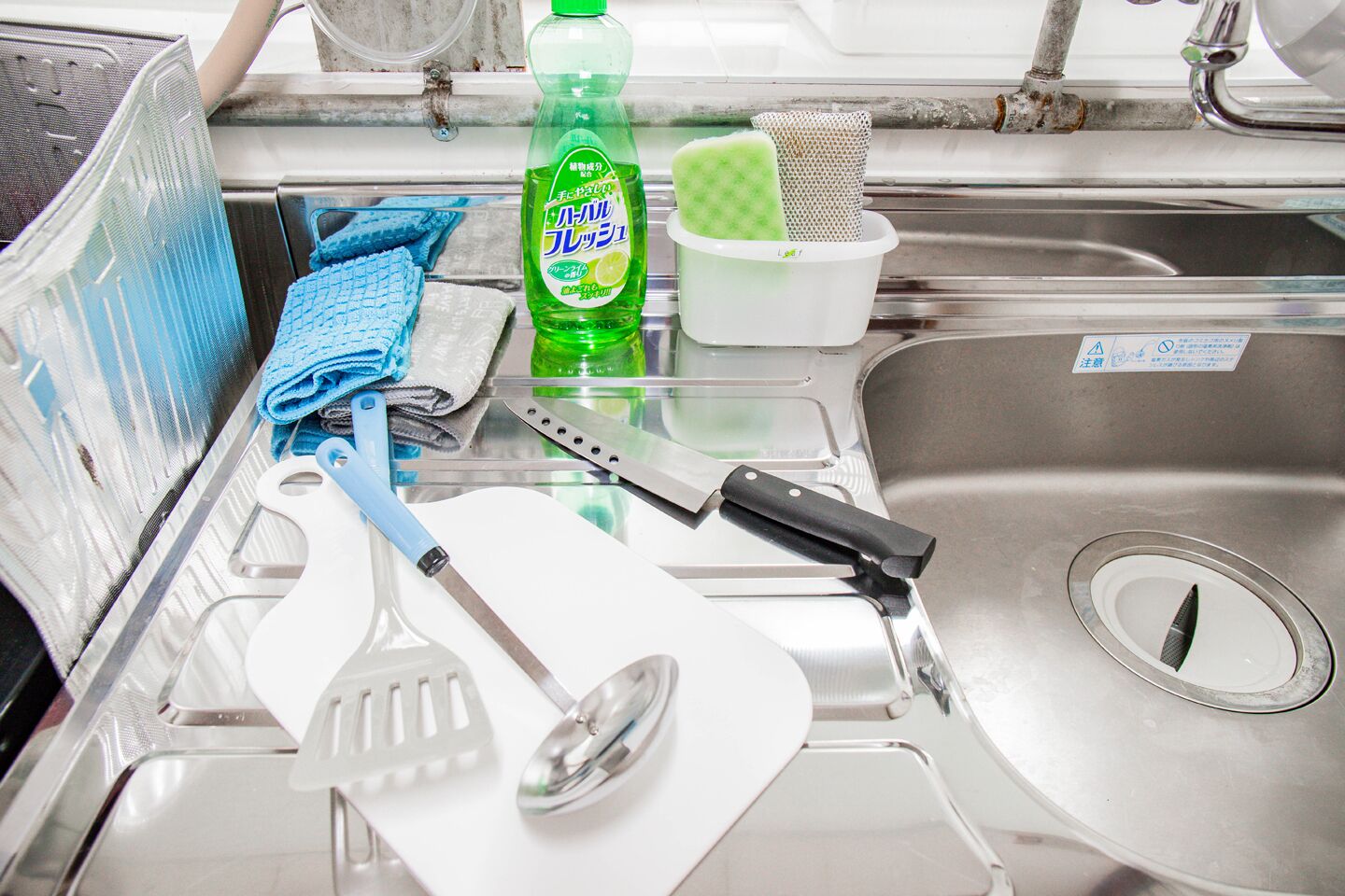 A kitchen sink area with a dish soap bottle, a sponge, a dish rack, and various kitchen utensils.