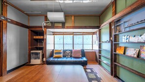 Una habitación acogedora con una mesa de madera, un sofá azul con cojines, una estantería y un ventanal que deja entrar luz natural.