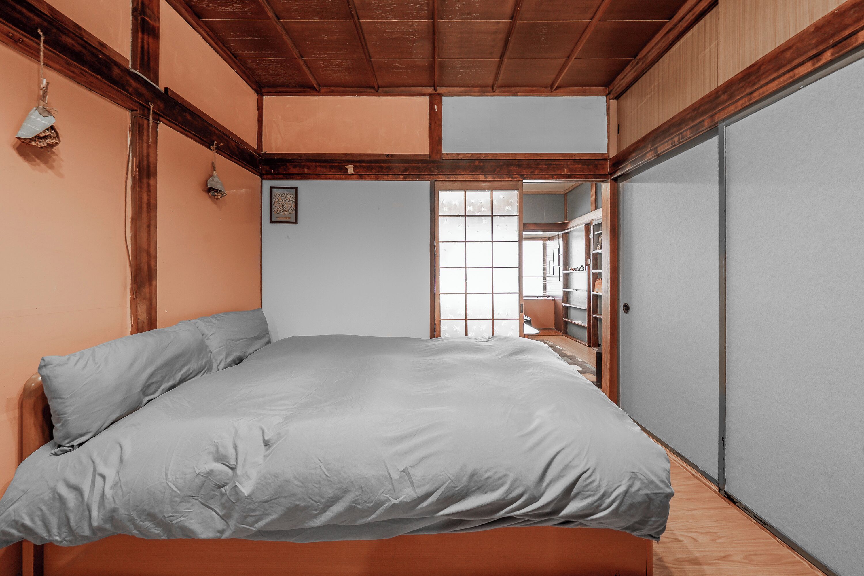 A bedroom with a large bed, wooden beams on the ceiling, a sliding door, and a view of a bathroom.