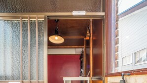 Un pasillo estrecho con una puerta de madera, una mesita con una lámpara colgante y una pared roja.