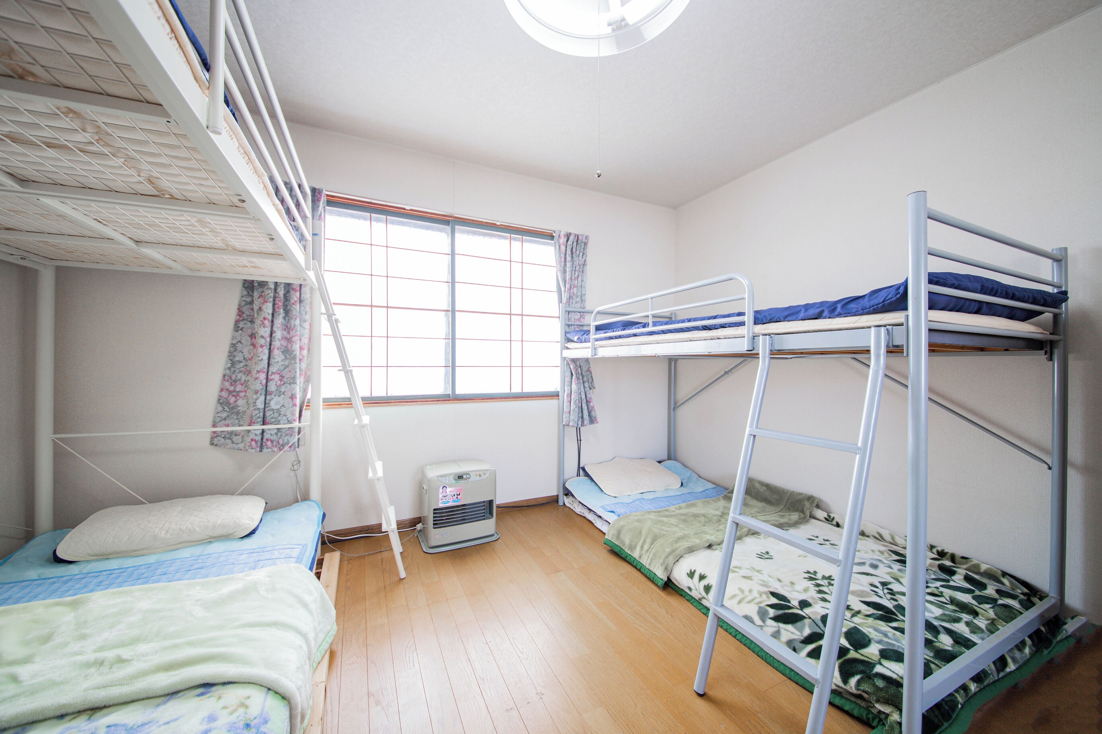 Un dormitorio con literas, una ventana con cortinas, un calentador y un ventilador de techo.