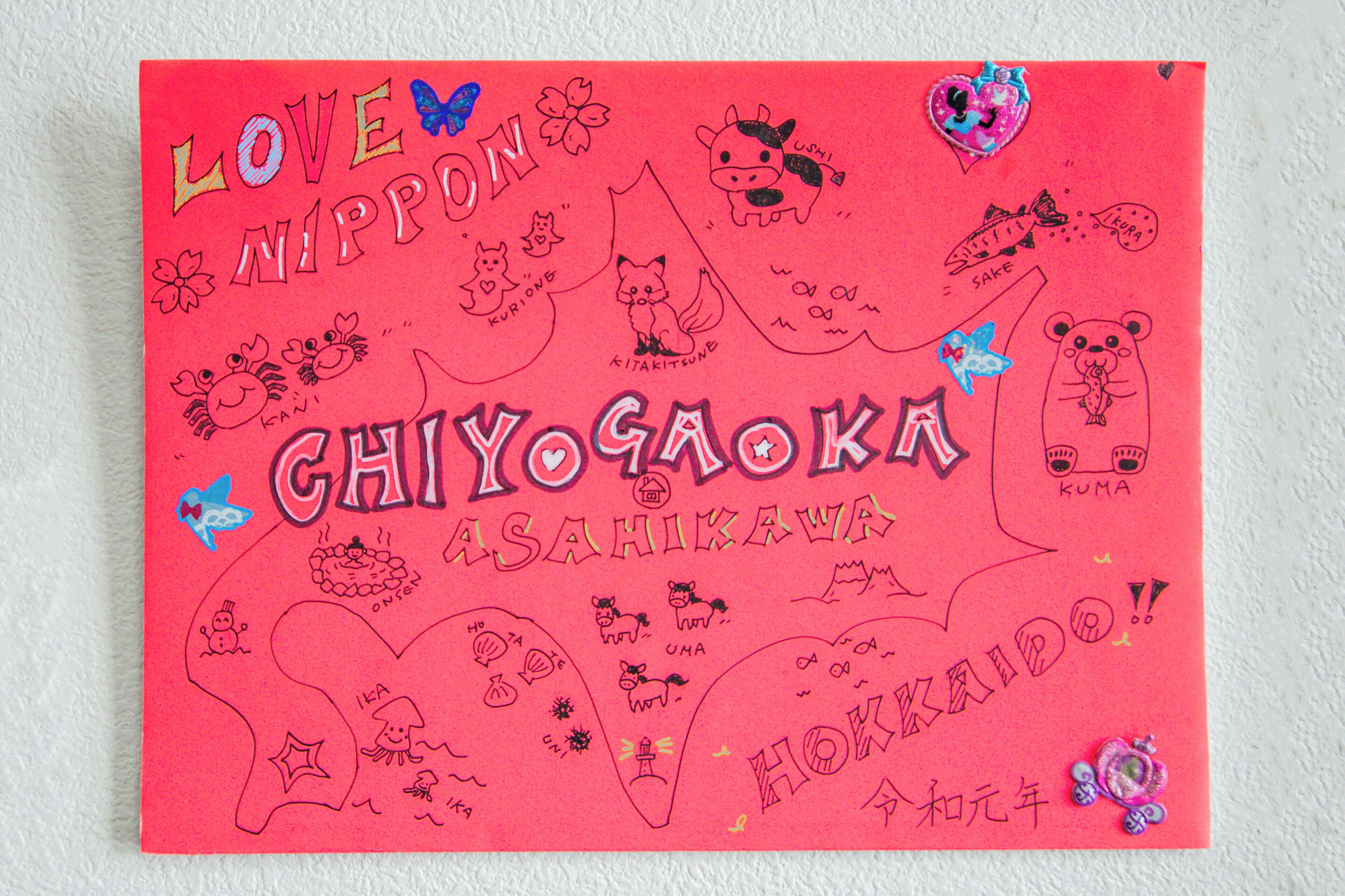 A vibrant red card with Japanese text and various doodles, including animals and symbols.