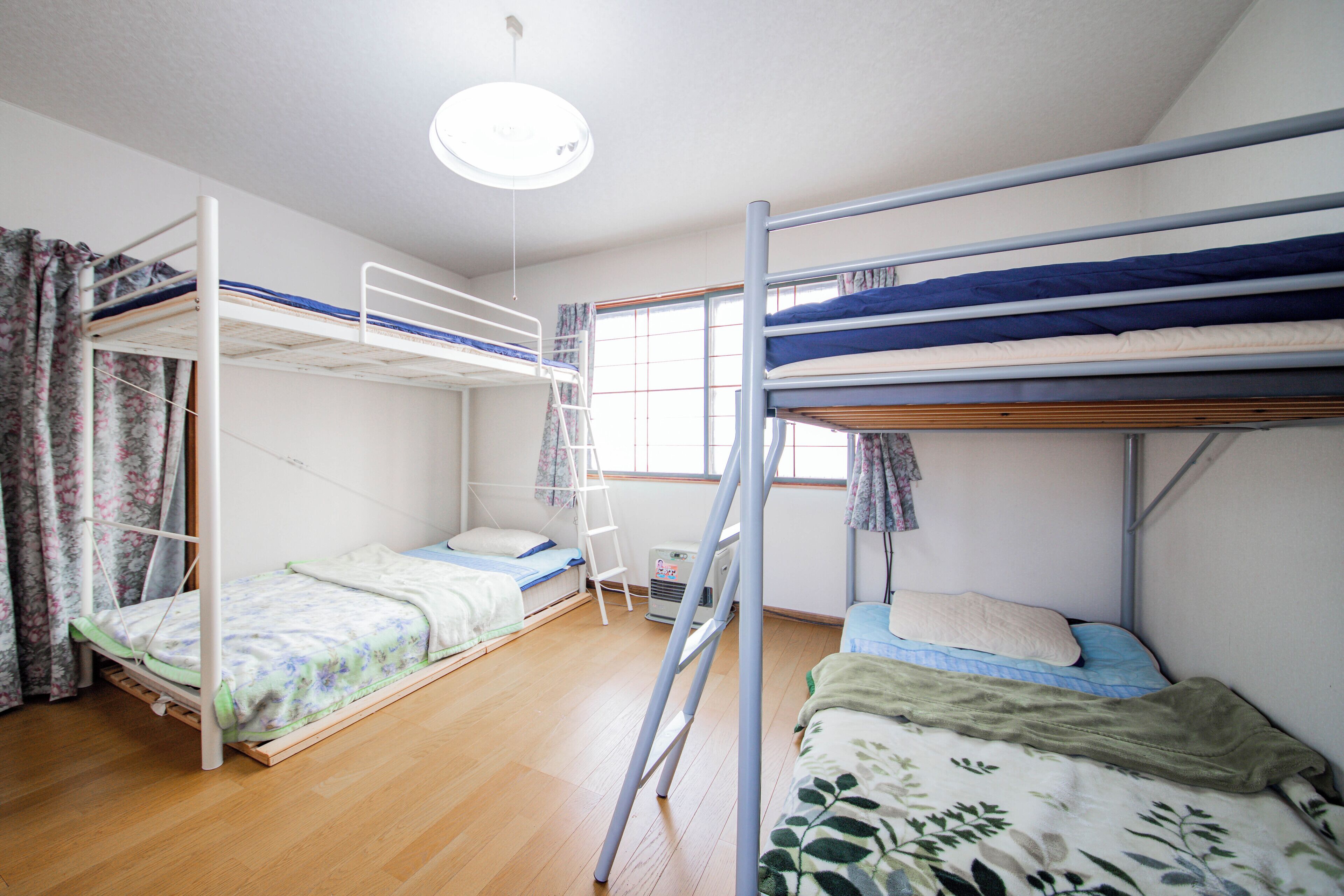 Ein Zimmer mit Etagenbetten, einer Leiter, einem Fenster mit Vorhängen und einer Deckenleuchte.