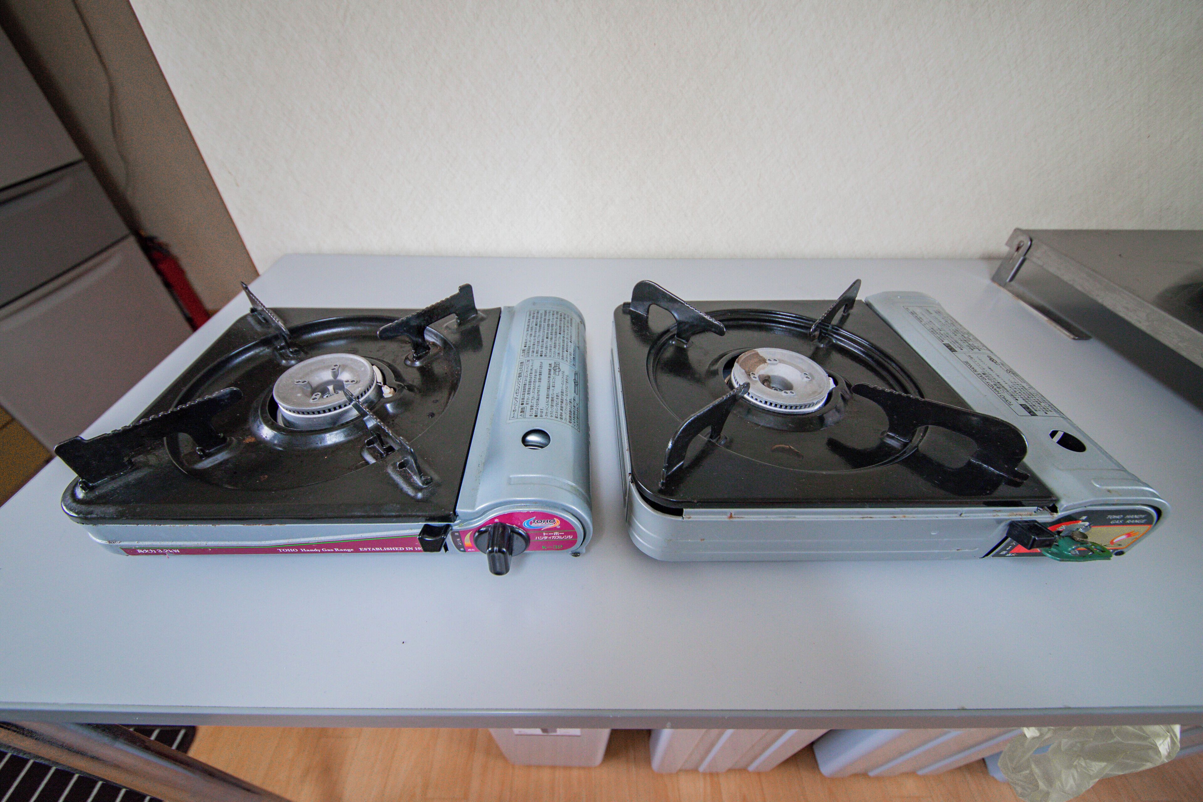 Two gas stoves on a white countertop with a white wall in the background.