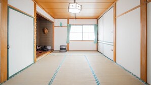 Ein traditioneller japanischer Raum mit Tatami-Böden, Schiebetüren, einem Deckenventilator und einem Fenster mit Vorhängen.