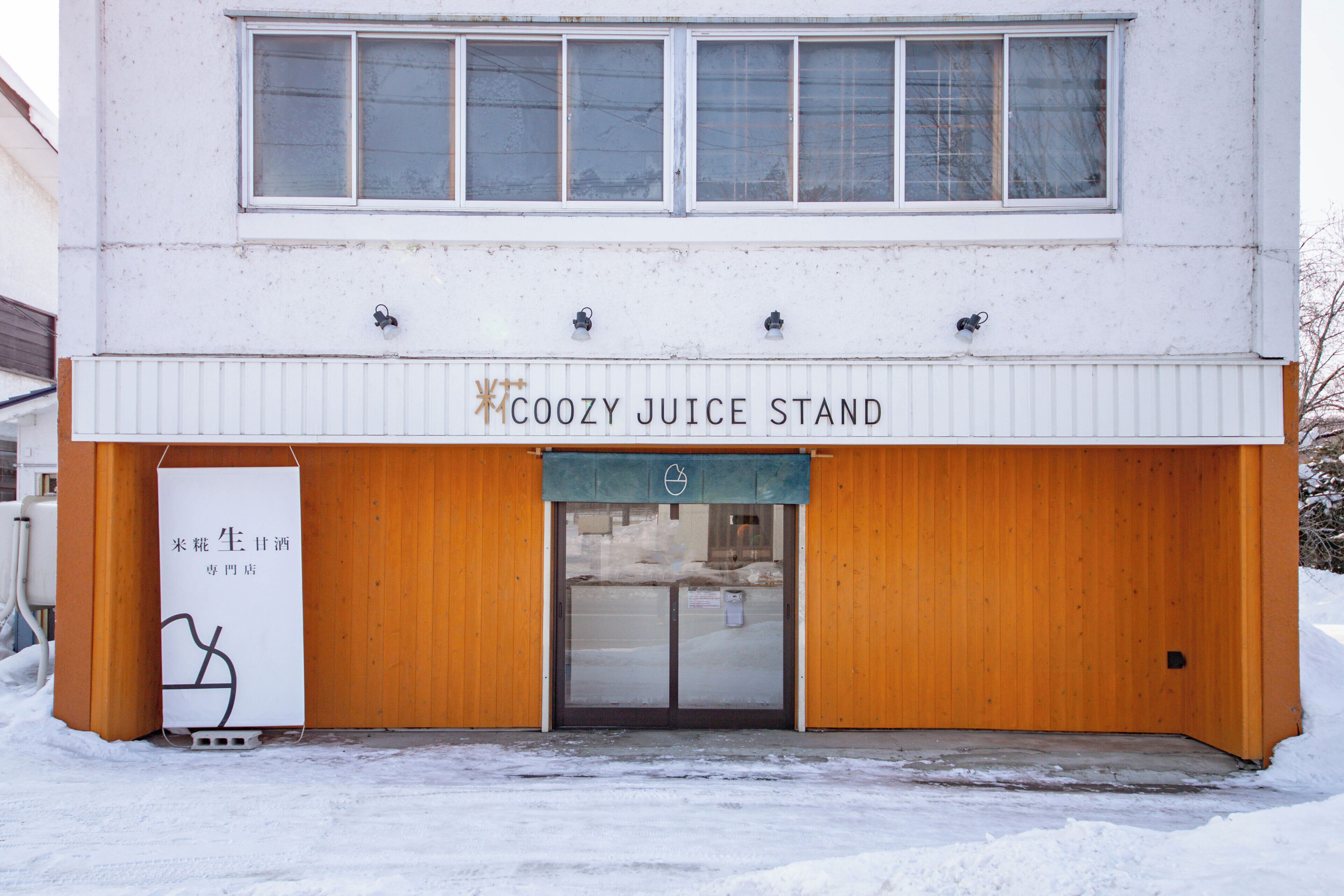 A building with a sign reading 'COOZY JUICE STAND' and a wooden door.