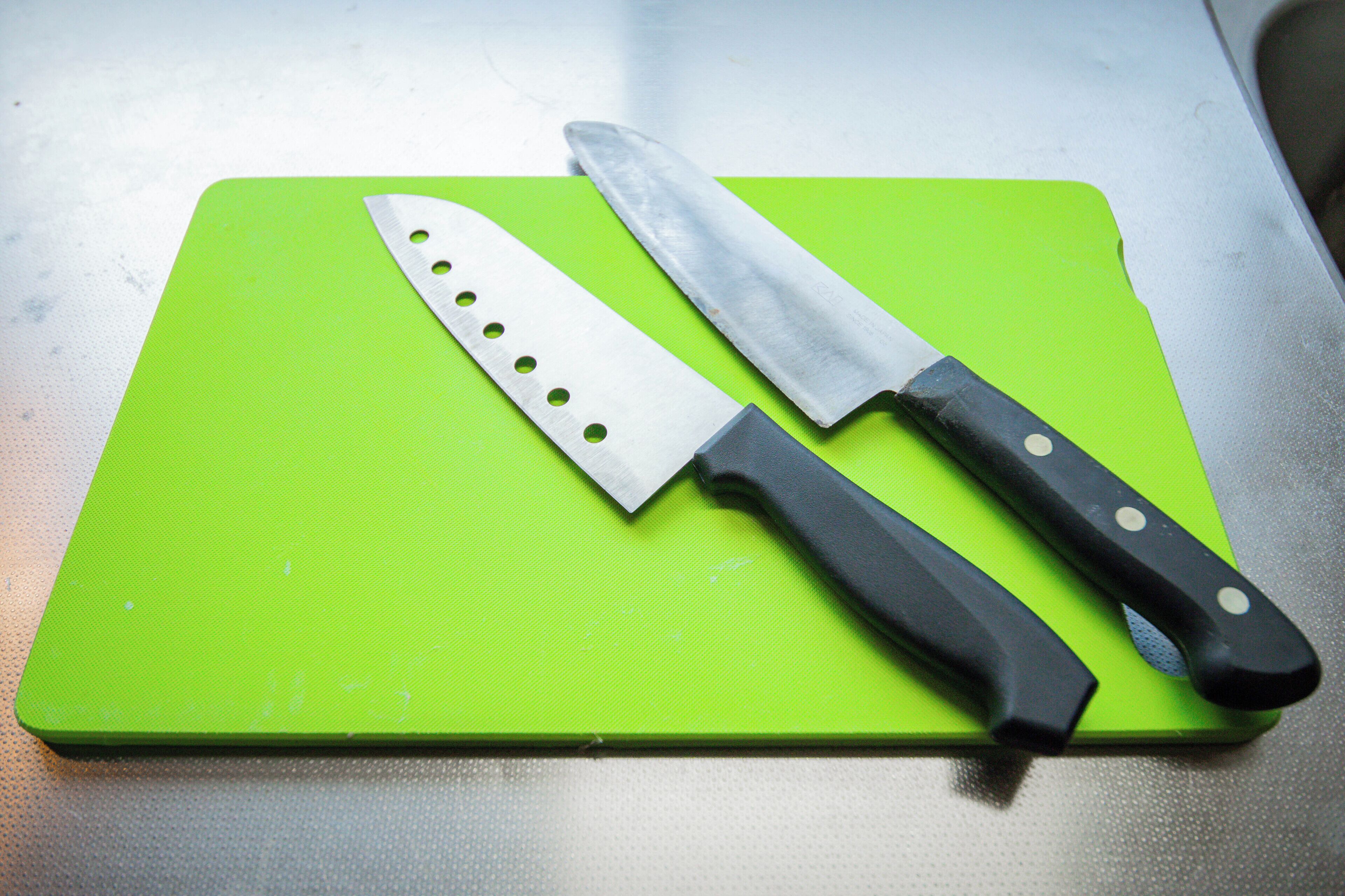 A green cutting board with two knives on it.