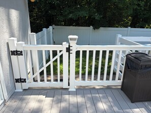 Une terrasse en bois avec une clôture blanche, une poubelle et un bâtiment blanc en arrière-plan.