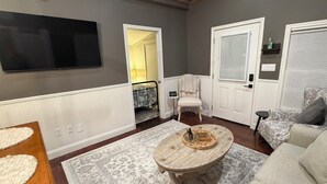 Ein Wohnzimmer mit einem an der Wand befestigten Flachbildfernseher, einem runden Couchtisch aus Holz, einem gemusterten Teppich, einer Couch und einem Sessel.