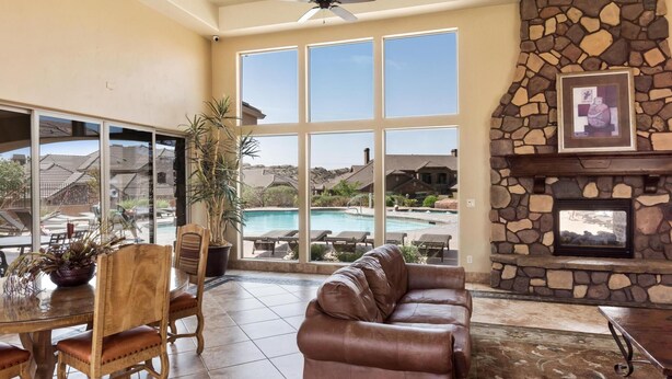 A spacious living area with a large window overlooking a pool, a stone fireplace, and a leather sofa.