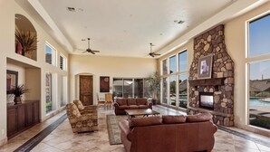 A spacious living area with a stone fireplace, large windows, and a pool view.