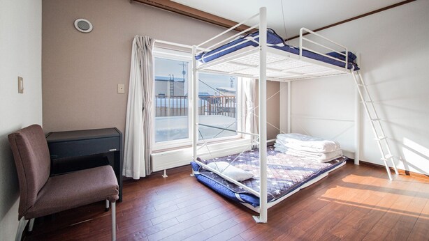 Ein Schlafraum mit Etagenbetten, einem Schreibtisch und Stuhl, einem Fenster mit Vorhängen und einem Holzboden.