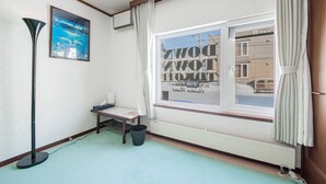 Ein Zimmer mit Fenster, einer Stehlampe, einem kleinen Tisch mit Stuhl und einem Heizkörper.