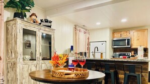 Una cocina con una mesa de comedor de madera, dos taburetes de bar, un armario con puertas de cristal y un microondas.