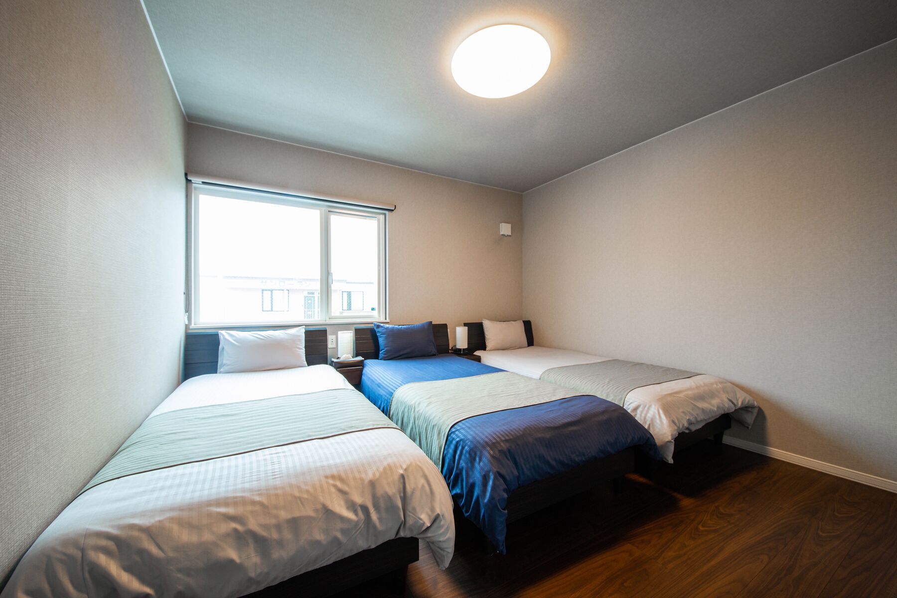 Ett hotellrum med tre enkelsängar, ett stort fönster och en taklampa.