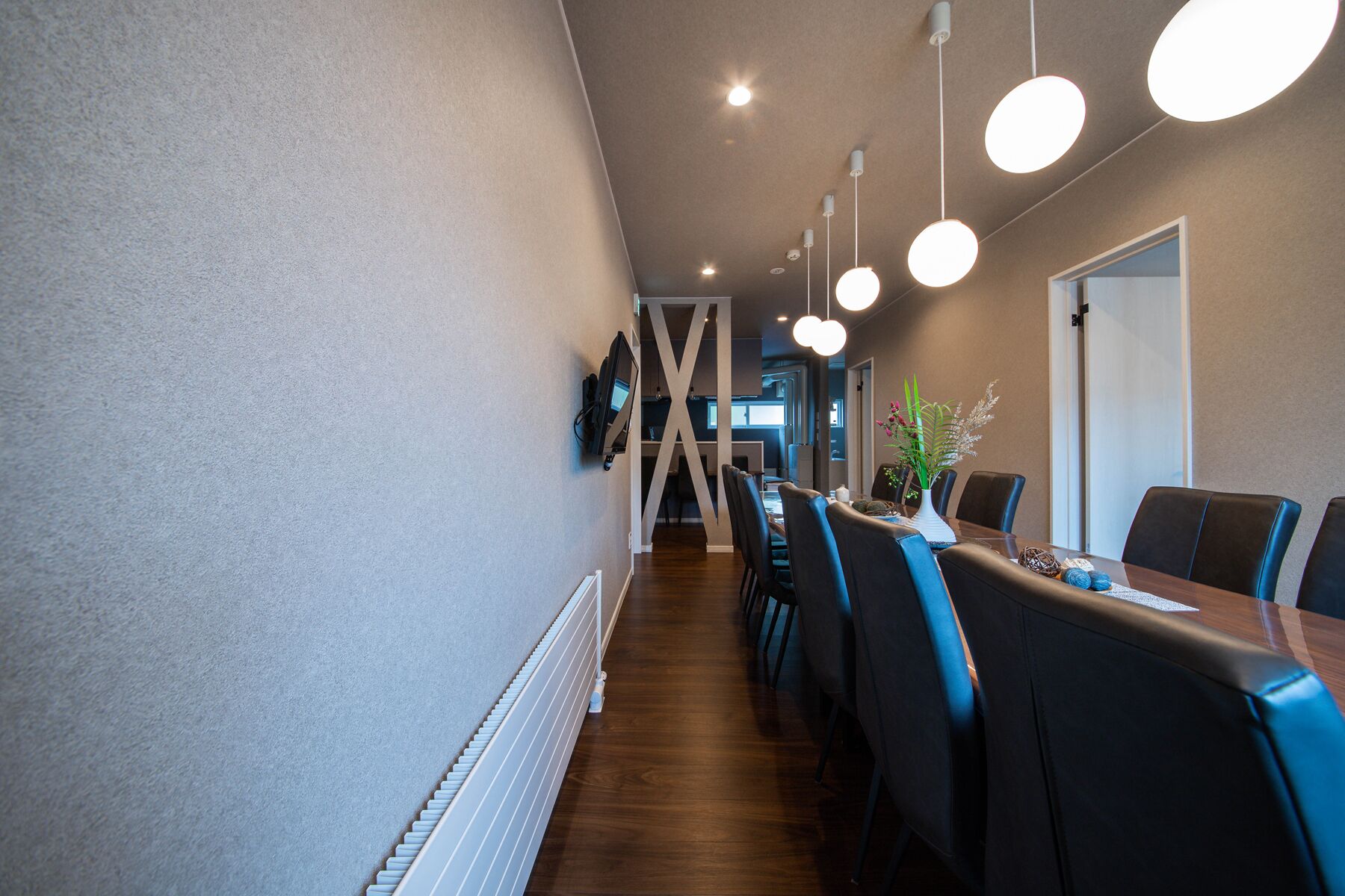 A modern dining area with a long table, dark chairs, and hanging pendant lights.