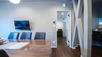 A conference room with a long table, chairs, a television, and a door with an exit sign.