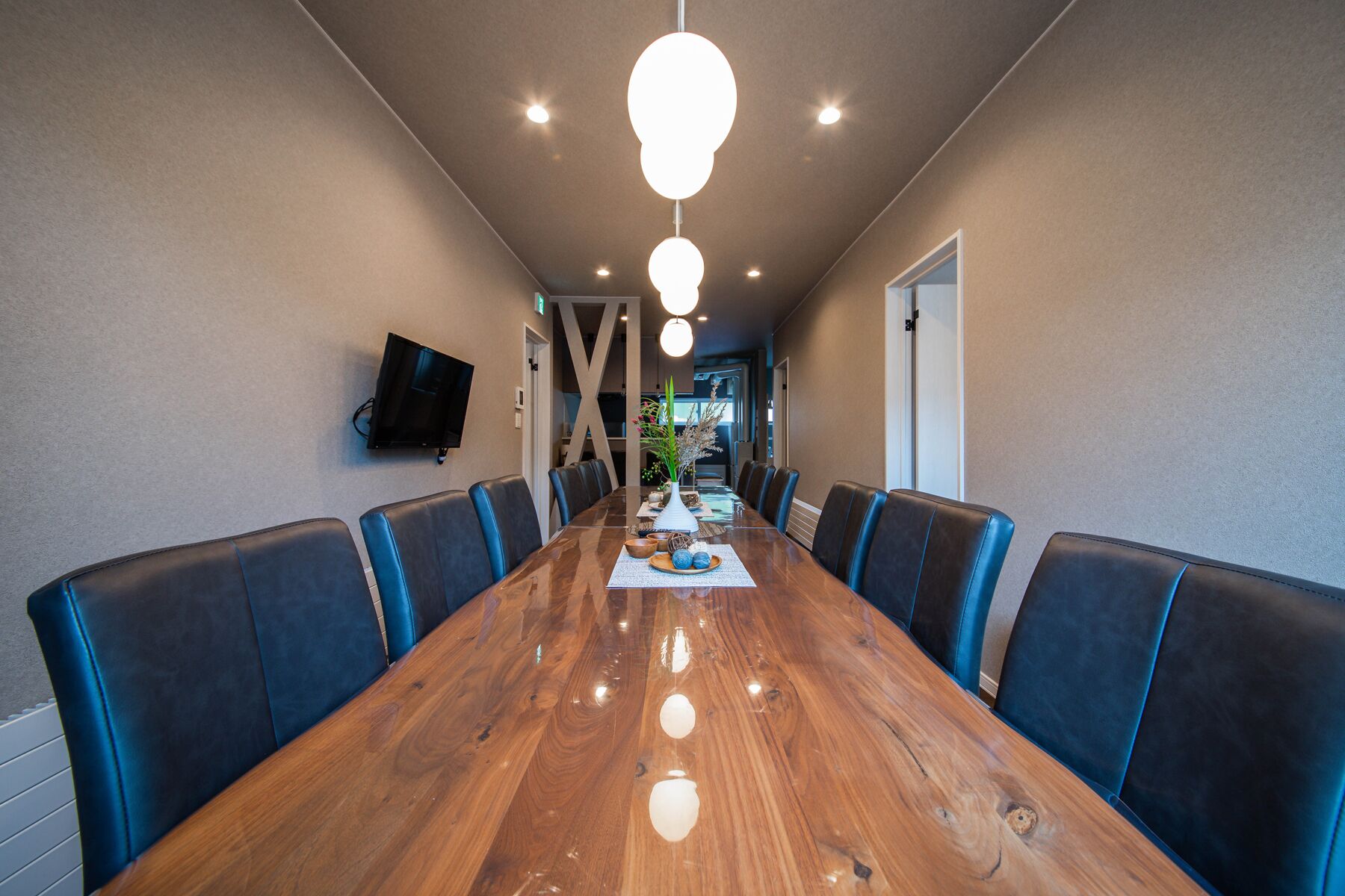 A conference room with a long wooden table, blue upholstered chairs, and a mounted TV on the wall.