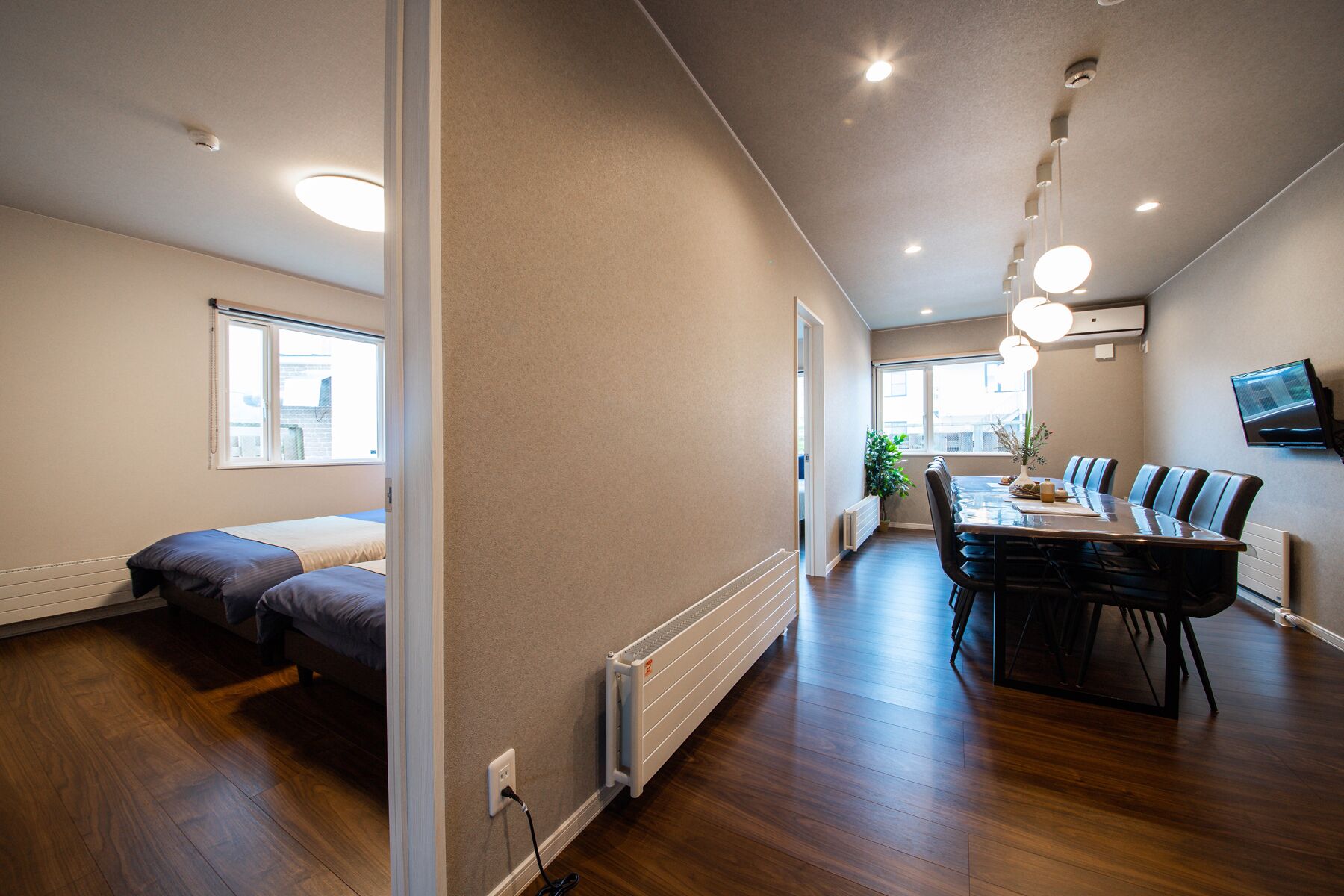 Un apartamento moderno con piso de madera, un comedor con mesa y sillas, una cama con ventana y un televisor montado en la pared.