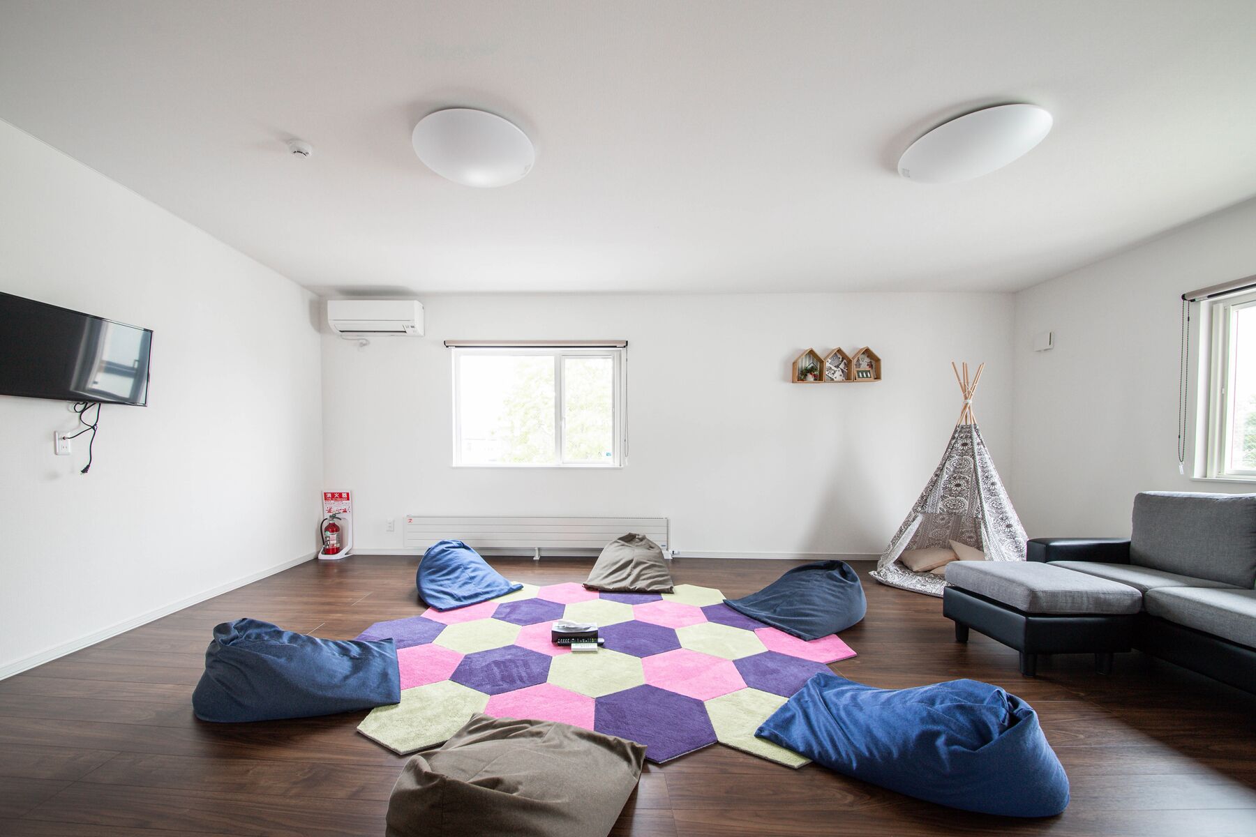 A spacious living room with a large window, a fireplace, a sofa, and a colorful hexagonal rug.