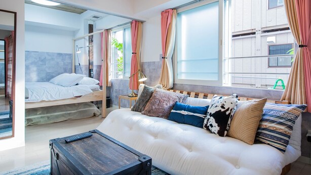 A modern bedroom with a bunk bed, a sofa with patterned cushions, and a bedside table with a lamp. - CLASSE TROIS (Sapporo)