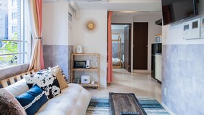 A modern living room with a sofa, a coffee table, and a TV. There is a kitchen area with a microwave and a refrigerator. - CLASSE TROIS (Sapporo)