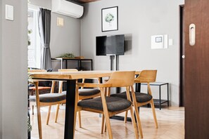 Un comedor moderno con una mesa y sillas de madera, un televisor de pantalla plana montado en la pared y una mesita auxiliar con una planta.
