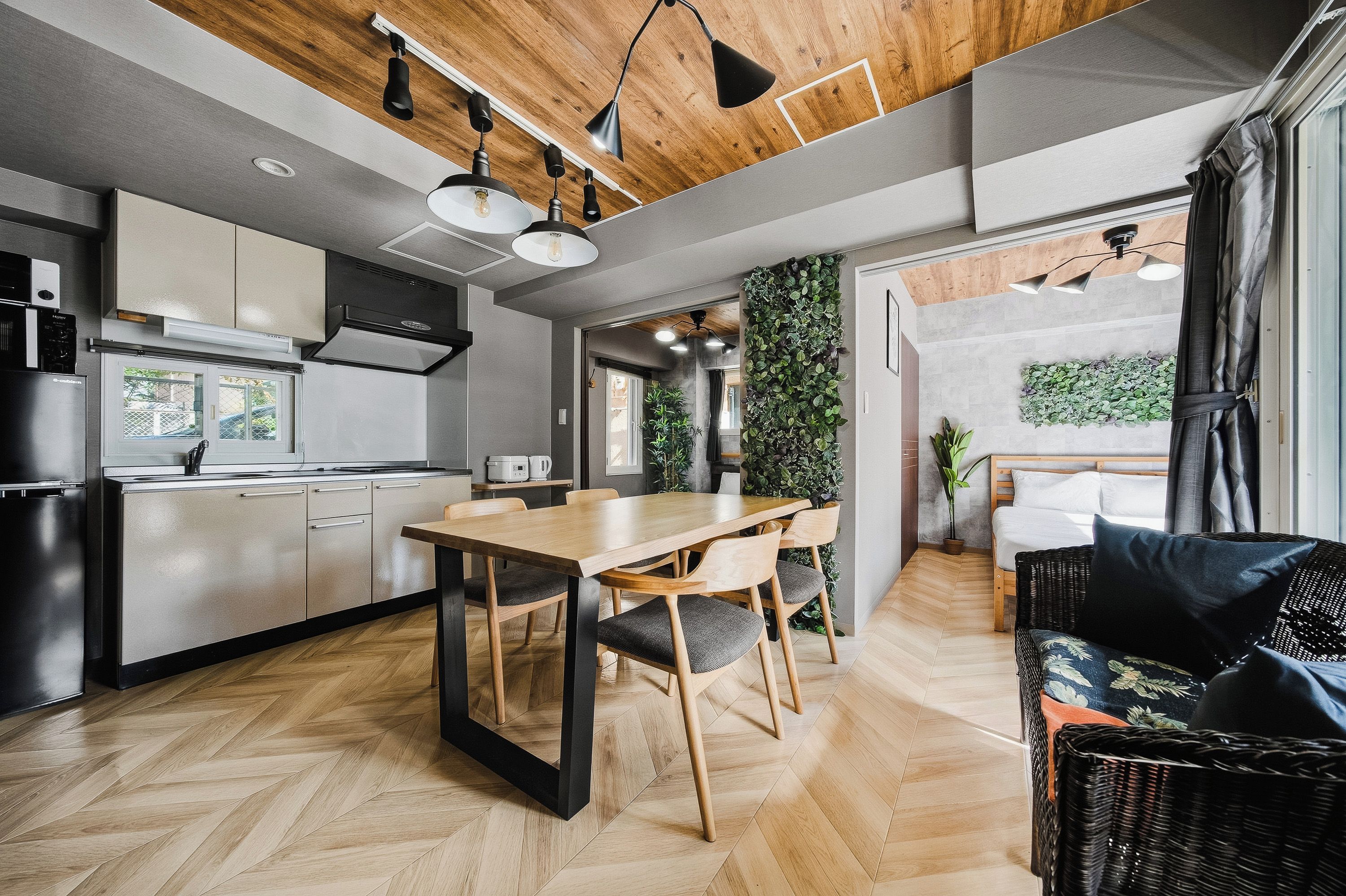 A modern kitchen with a dining area, wooden flooring, and a living space with a sofa and a wall-mounted plant.