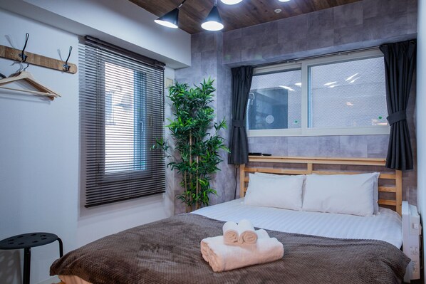 A bedroom with a bed, a window with blinds, a plant, and a towel on the bed. - CLASSE CINQ (Sapporo)