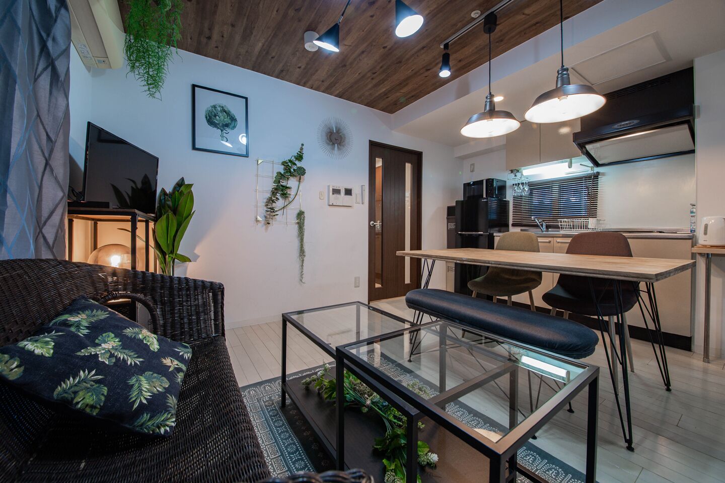 A modern living room with a glass coffee table, a dark wicker sofa, and a dining area with a wooden table and chairs.